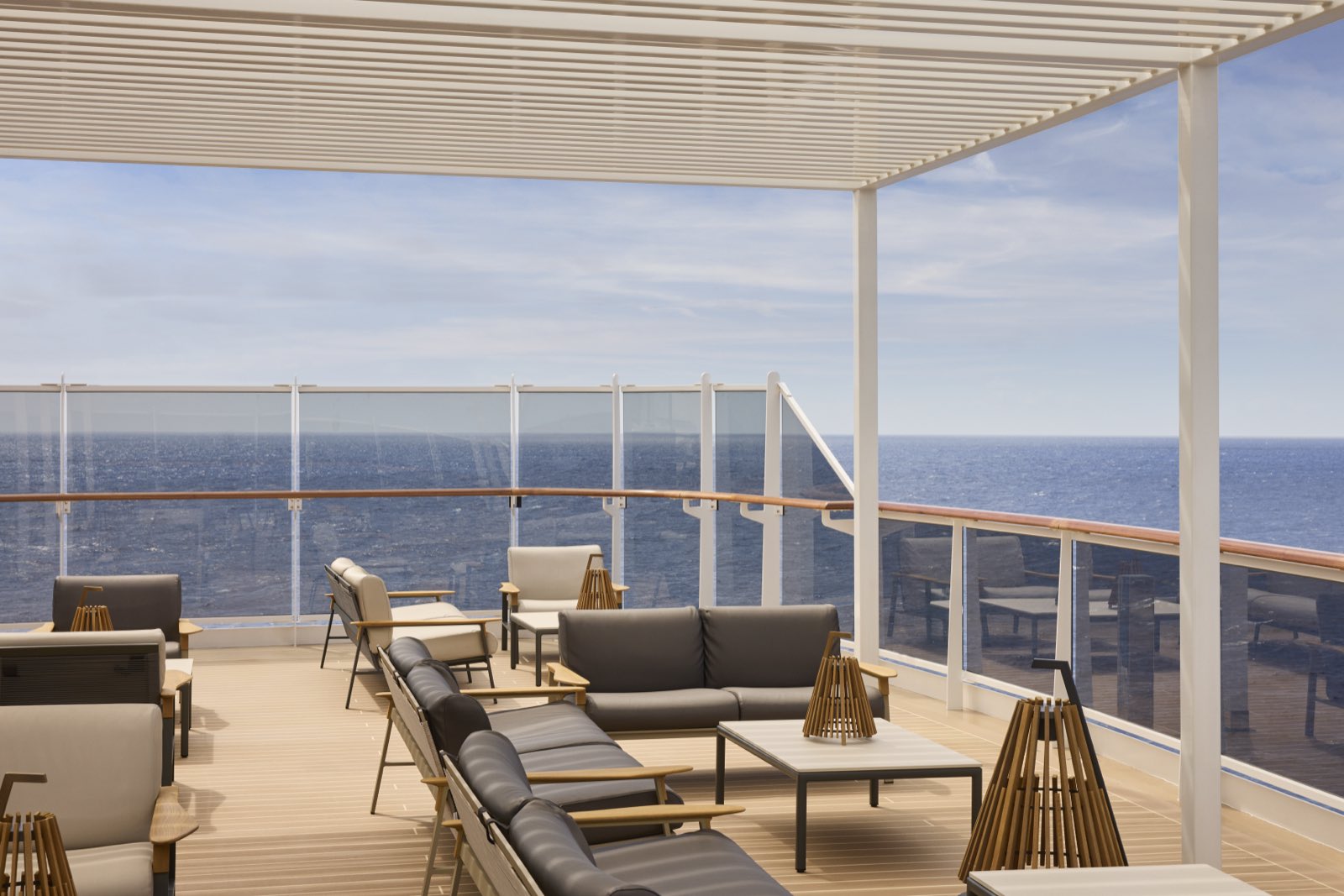 Überdachte Lounge an Deck eines Explora-Schiffs mit Sesseln, Sofas und Blick über die Reling aufs Meer