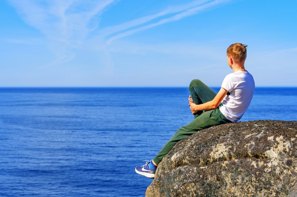 A boy sitting on the top of the mountain and enjoying Norway view above sea and mountains.